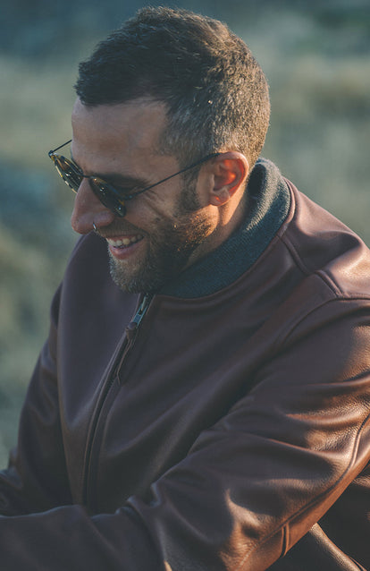 A man luaghing, wearing a brown leather jacket.