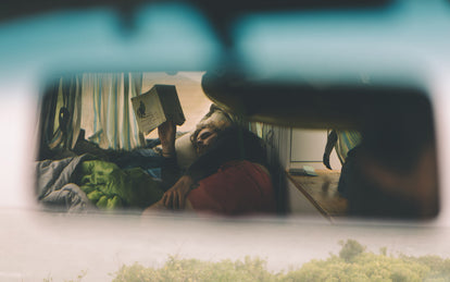 Shot through the rearview mirror of someone reading a book, lying in the back of a campervan.