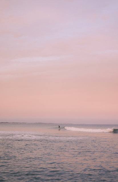 Surfing some small glassy waves, with the pink sky reflected.
