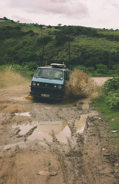 A VW camper fording a muddy creek.