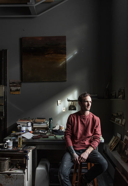 Tim sitting, wearing the crewneck in brick red terry with the morse pant in charcoal.