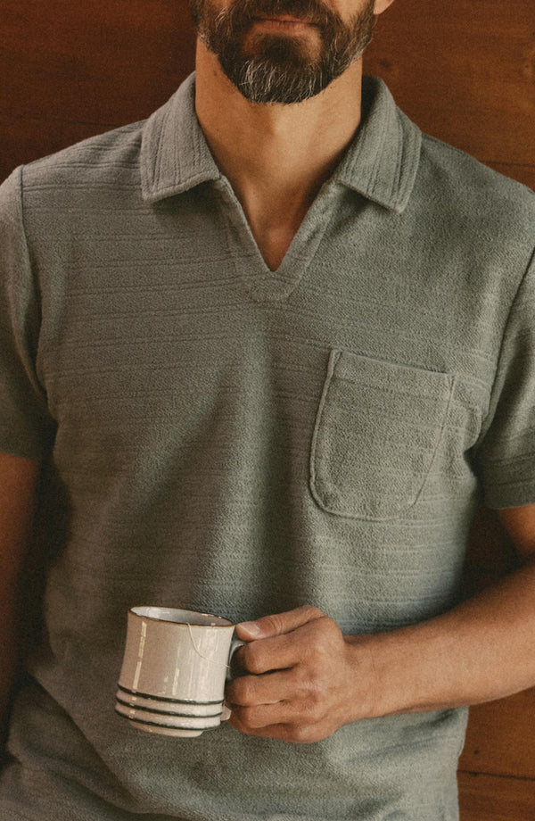 fit model holding a coffee wearing The Meridian Polo in Faded Pine