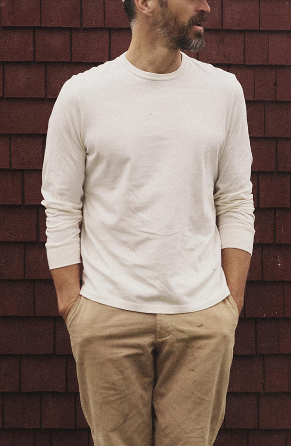 fit model leaning against the wall wearing The Organic Cotton Long Sleeve Tee in Vintage White