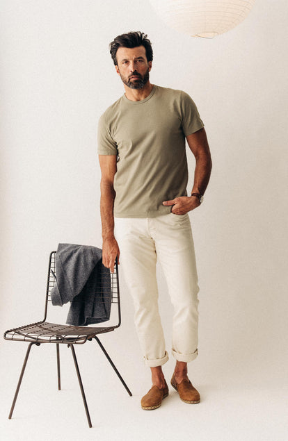 fit model leaning against a chair wearing The Organic Cotton Tee in Sage