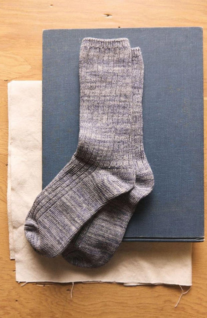 The Ribbed Sock in Ash melange on a textured surface