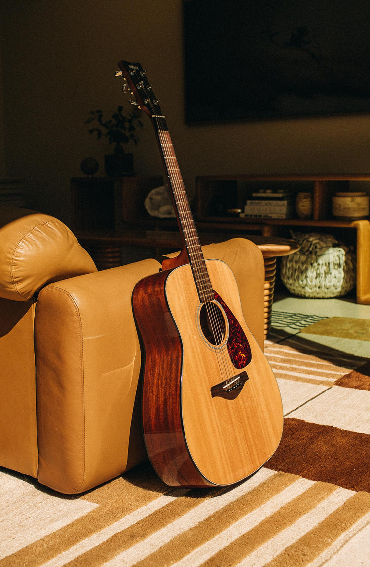 guitar standing against a leather couch