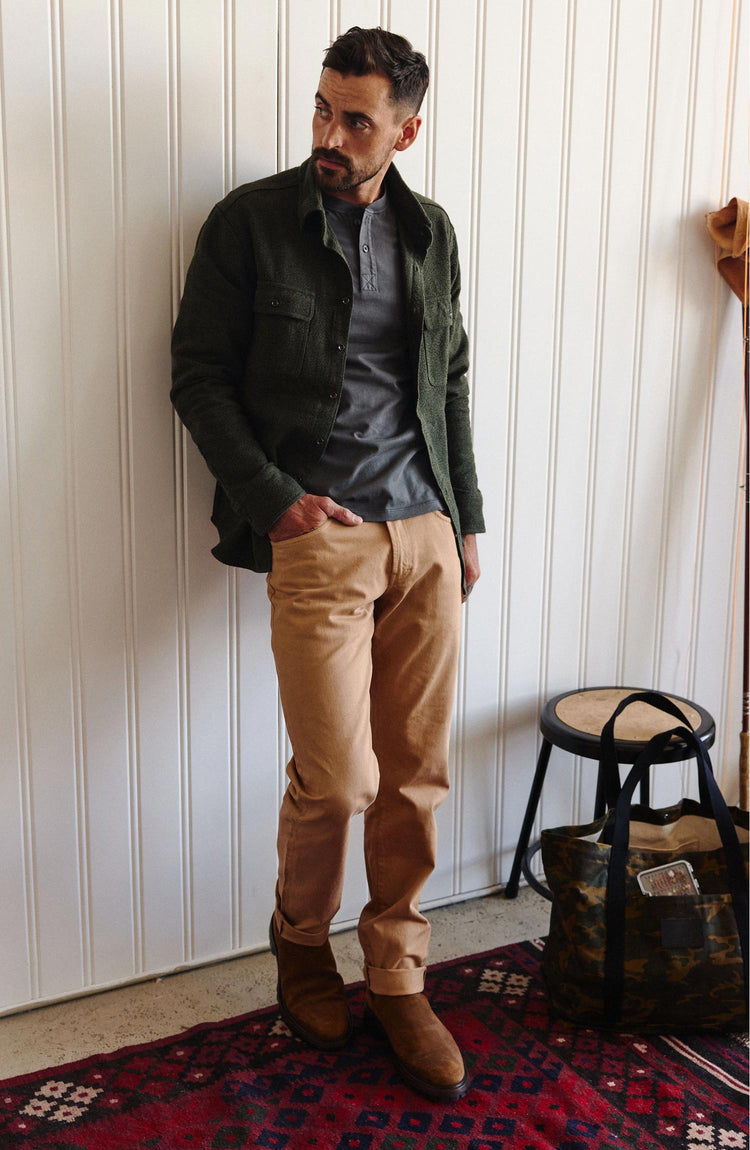 fit model leaning against the wall wearing The Slim All Day Pant in Tobacco Selvage Denim