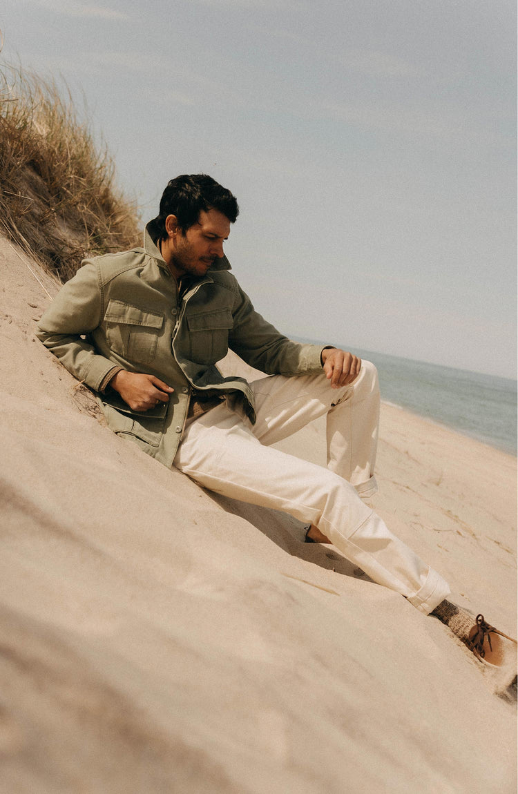 fit model sitting on sand dunes wearing The Surplus Jacket in Field Olive Reverse Sateen