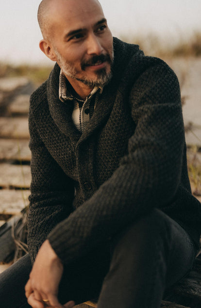 fit model sitting wearing The Fisherman Shawl Cardigan in Heather Coal Merino