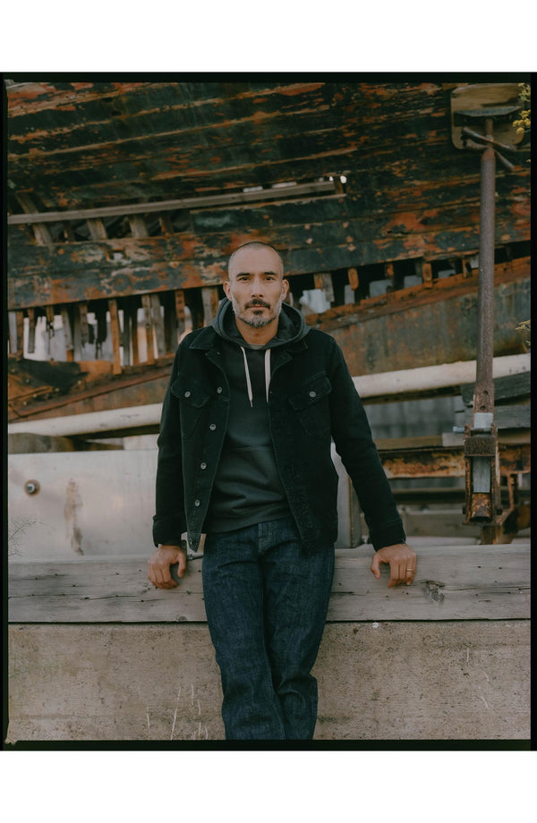 fit model leaning against the wall wearing The Long Haul Jacket in Black Indigo Waffle