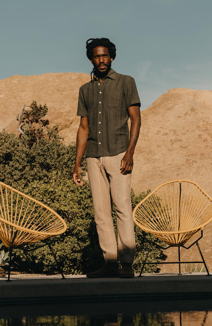 fit model standing next to chairs wearing The Short Sleeve California in Heather Olive Pointelle Stripe
