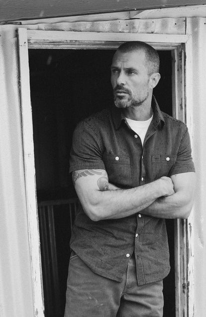fit model leaning against the wall wearing The Short Sleeve Utility Shirt in Roped Indigo