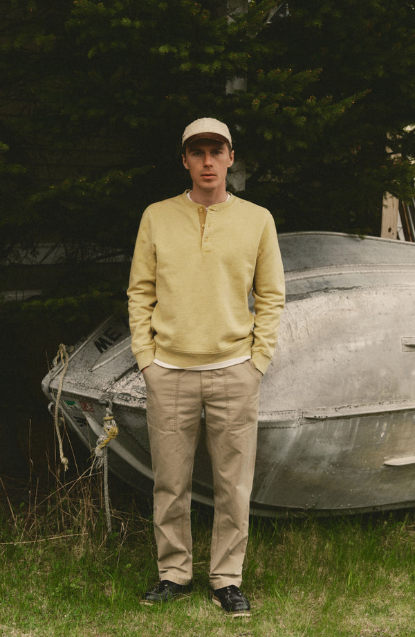 fit model leaning against a boat wearing The Breakwater Pant in Field Khaki Ripstop