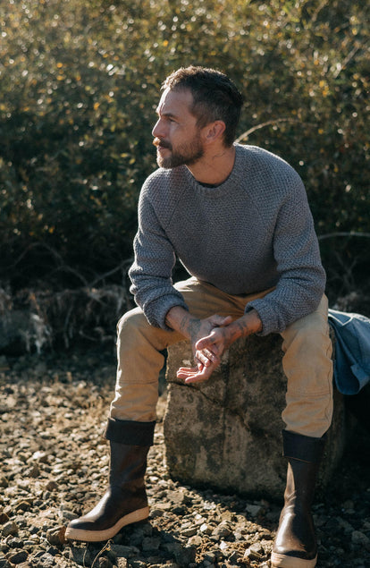fit model sitting on a rock wearing The Fisherman Sweater in Blue Melange