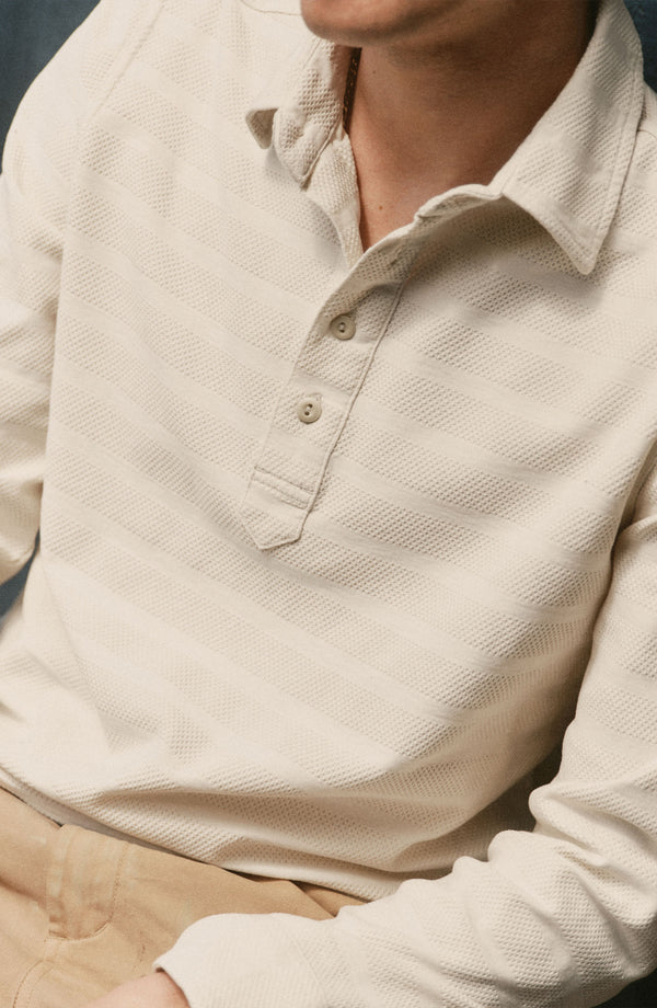 fit model sitting wearing The Long Sleeve Polo in Vintage White Knit Stripe