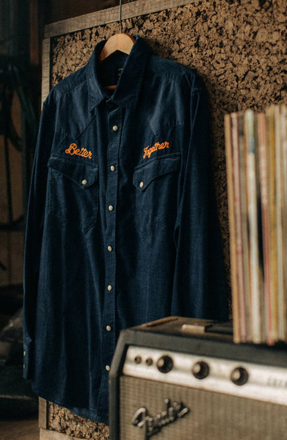 The Western Shirt in Better Together hanging on a cork wall next to a vintage stereo speaker