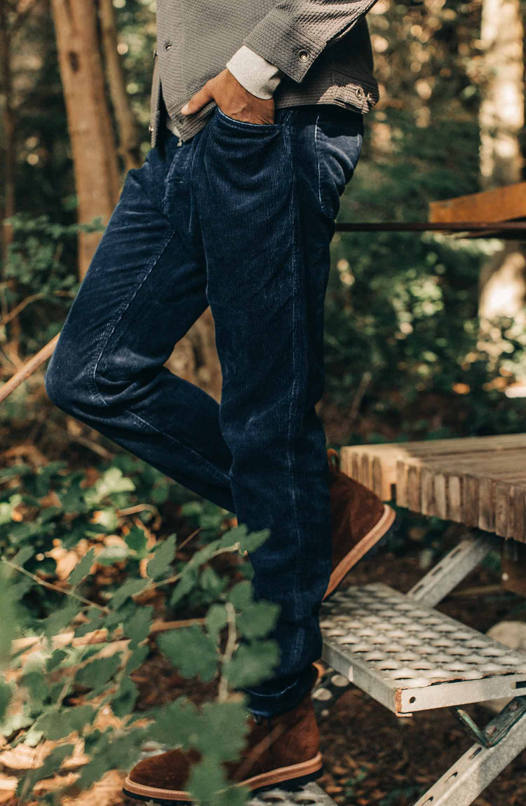 our fit model wearing the indigo cord camp pants near a house in the woods—split show with two images