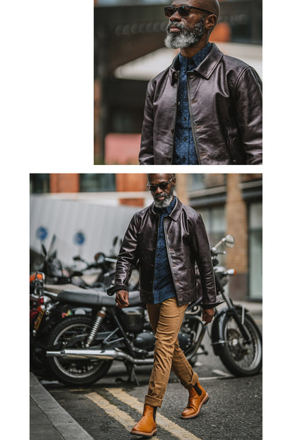 Efe posing with his leather jacket tucked under his arm, leaning against a railing that has bikes secured to it.