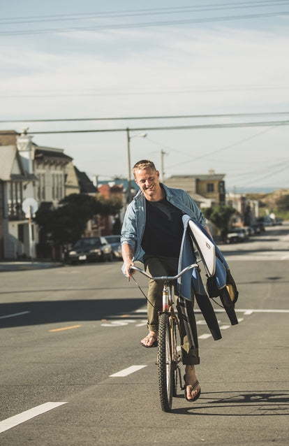 Our guy on a bike, in his Jack, carrying his surfboard and gear. Our man.