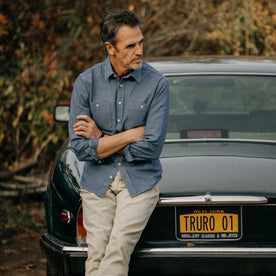 fit model leaning against a car in The Utility Shirt in Washed Indigo Herringbone