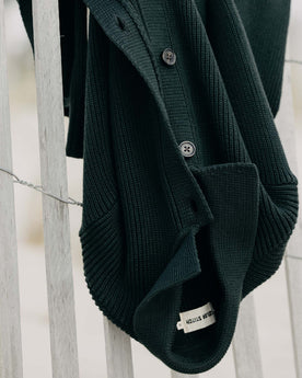 The Harbor Sweater Jacket in Black Pine Heather hanging on a fence, Knits by Taylor Stitch