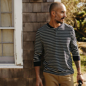 fit model leaning on a house wearing The Organic Cotton Henley in Rinsed Indigo Stripe