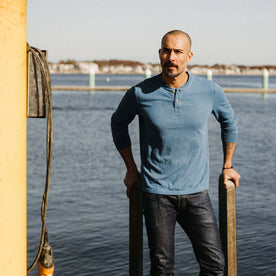 fit model standing on a dock wearing The Organic Cotton Henley in Washed Indigo
