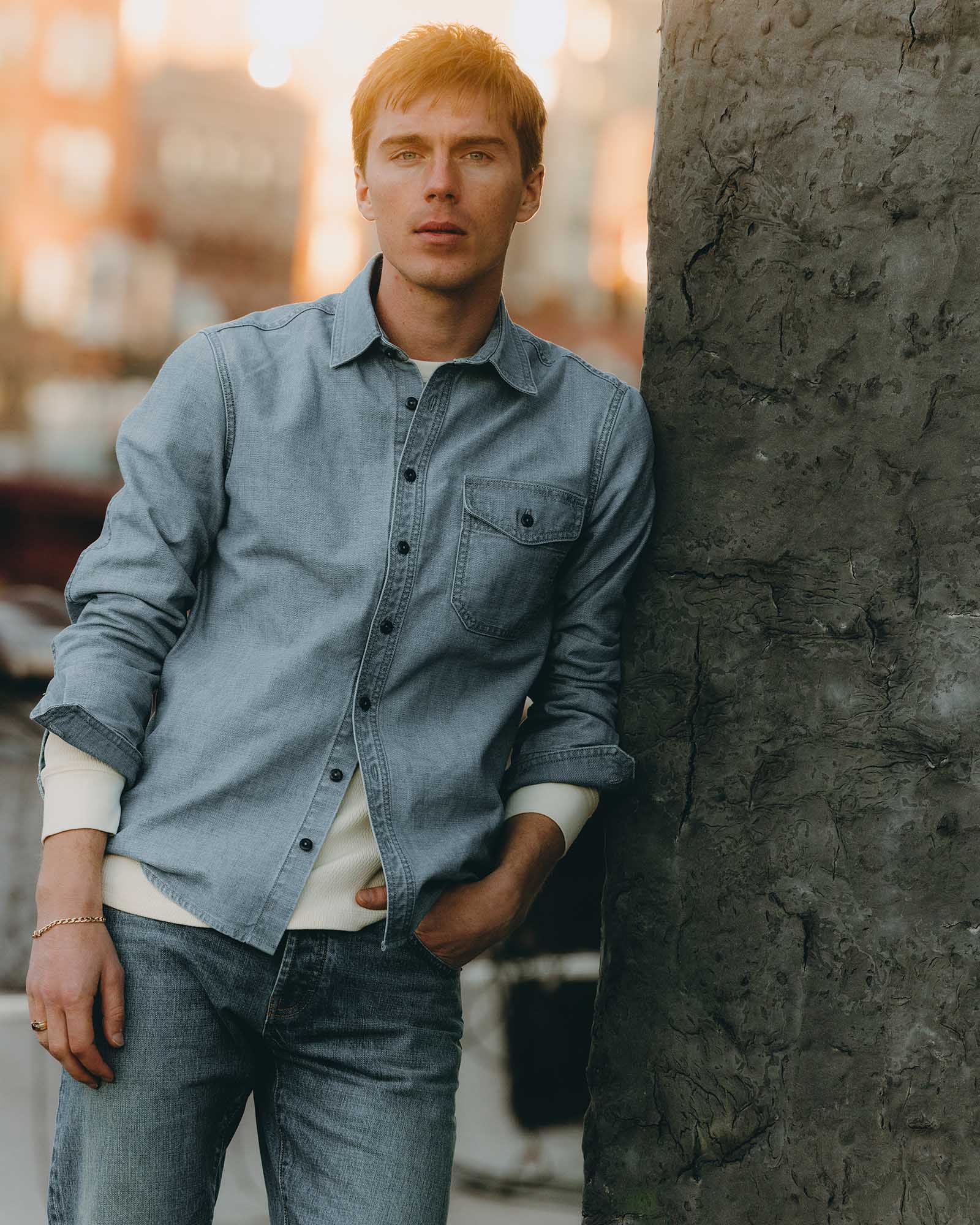 fit model leaning against a tree wearing The Cadet Shirt in Washed Indigo Oxford, Wovens by Taylor Stitch