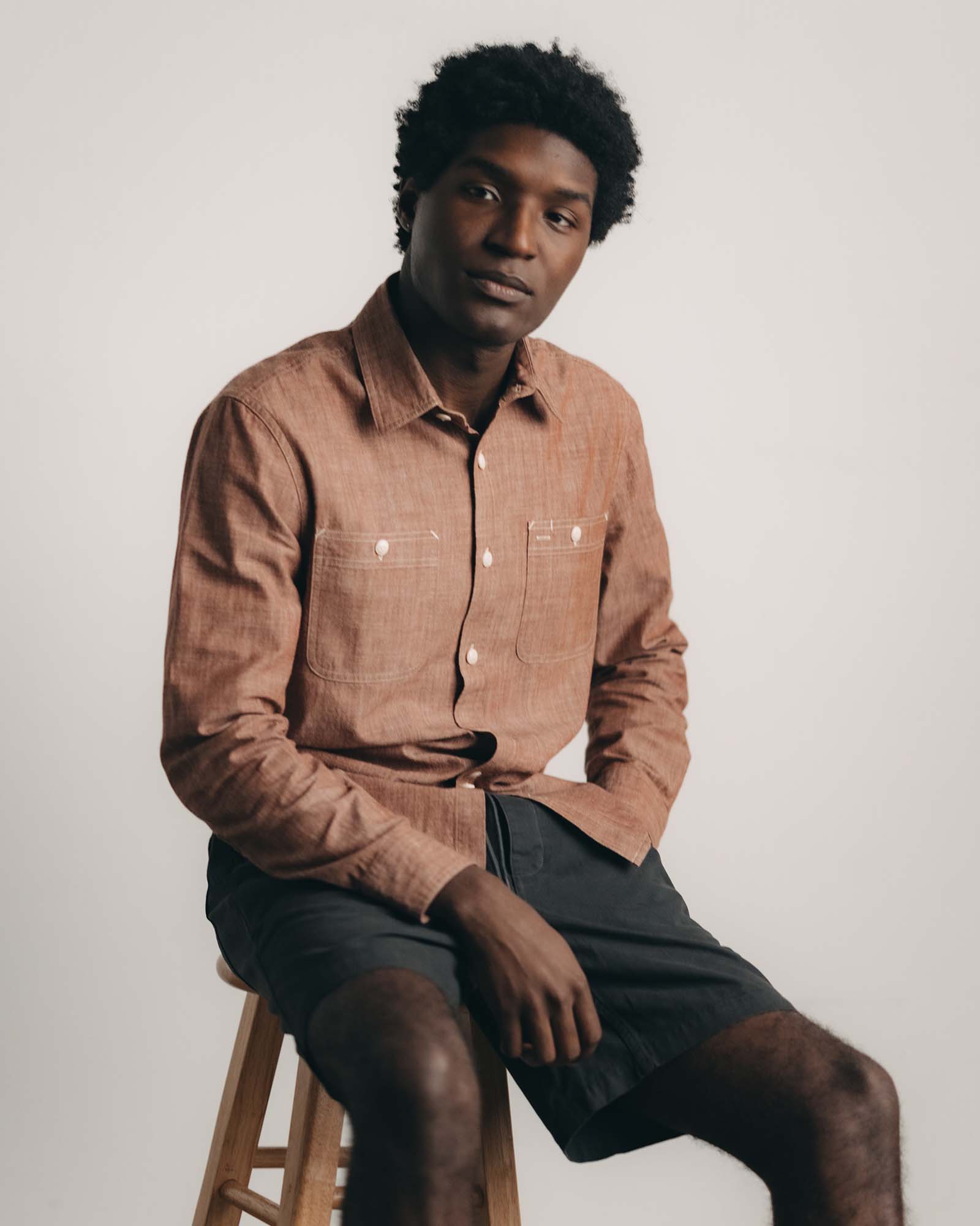 fit model sitting wearing The Foundry Shirt in Brick Chambray, Wovens by Taylor Stitch