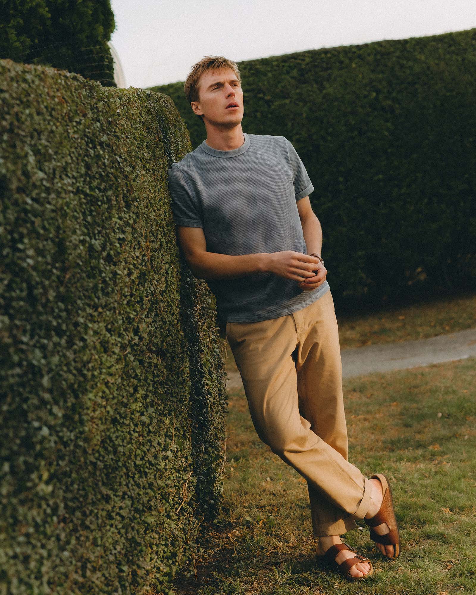fit model leaning against a hedge wearing The Organic Cotton Short Sleeve Crew in Washed Blue Waffle, Knits by Taylor Stitch