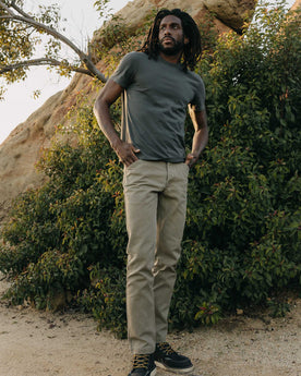 fit model posing next to a bush wearing The Organic Cotton Tee in Faded Black, Knits by Taylor Stitch