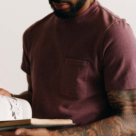 fit model holding a book wearing The Heavy Bag Tee in Dried Cherry