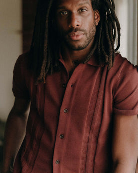 fit model leaning against the wall wearing The Button Down Polo in Dried Cherry Stripe, Knits by Taylor Stitch