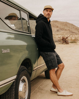 fit model leaning against a car wearing The Tommie Short in Faded Black Broken Twill, Bottoms by Taylor Stitch