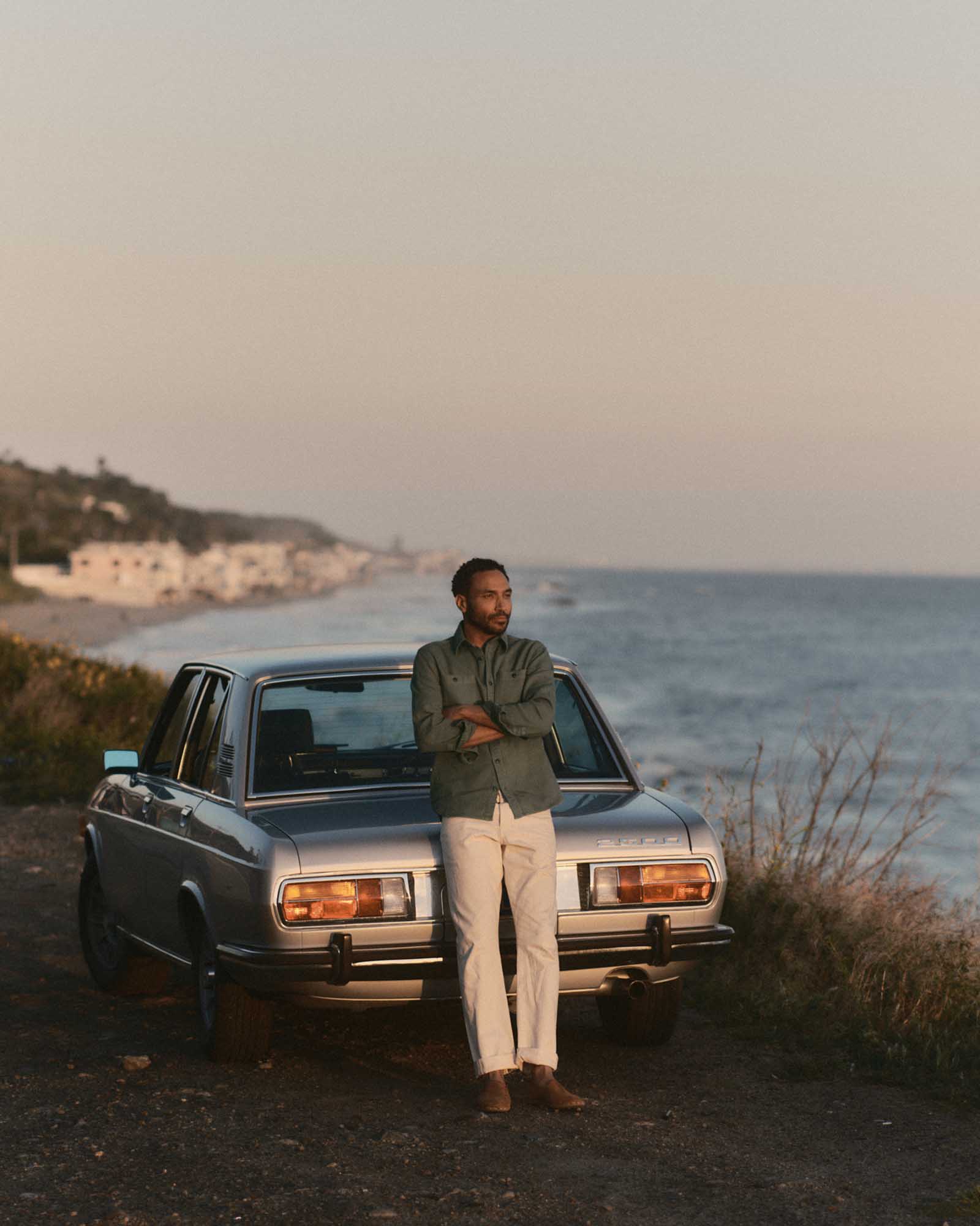 fit model leaning against a car wearing The Dispatch Shirt in Smoked Olive Broken Twill, Wovens by Taylor Stitch