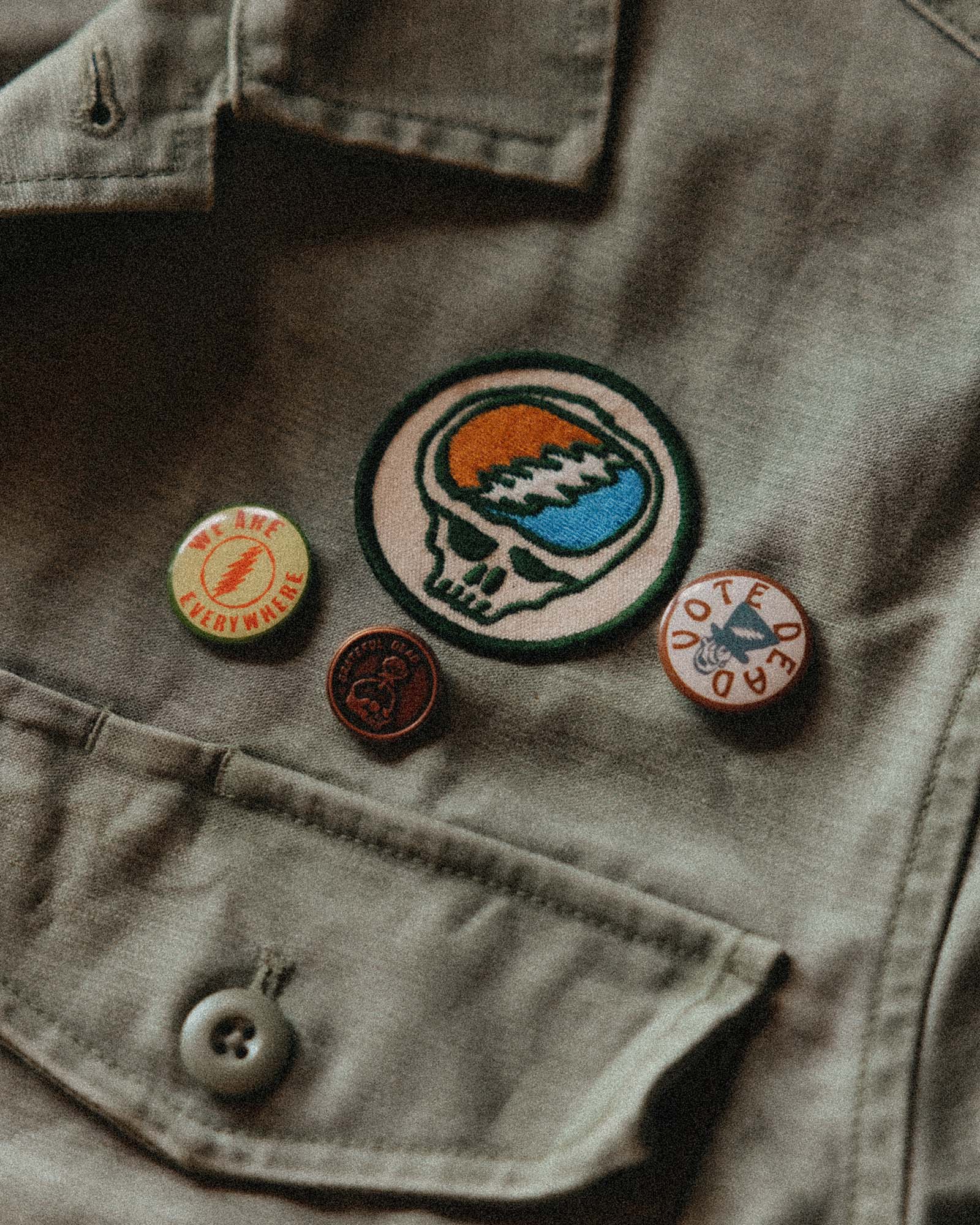 Close-up of a jacket with various pins and patches on a textured background, Accessories by Taylor Stitch