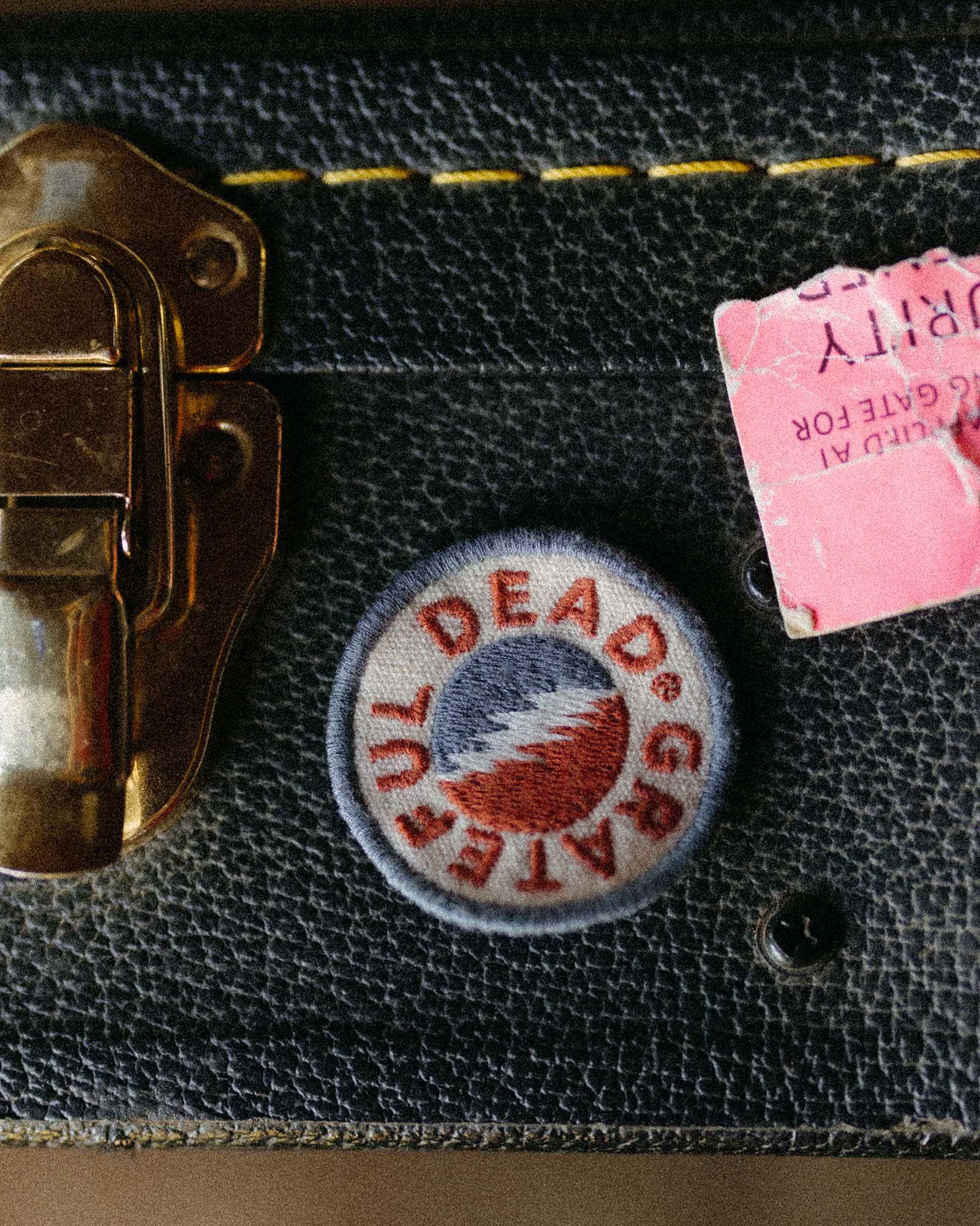 Close-up of a suitcase with a ' grateful dead' patch and a pink tag., Accessories by Taylor Stitch