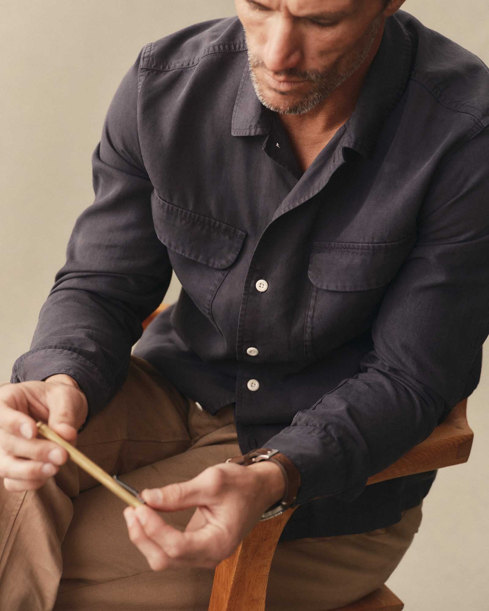 fit model sitting wearing The Shore Shirt in Navy Tencel, Wovens by Taylor Stitch