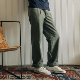 fit model leaning against the wall wearing The Matlow Pant in Dried Sage Pigment Herringbone