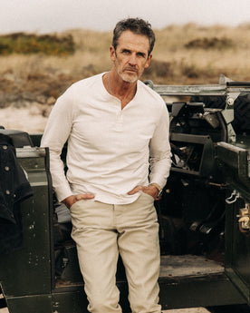 fit model leaning on his leg wearing The Organic Cotton Henley in Vintage White, Knits by Taylor Stitch