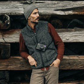 fit model leaning against the wood wearing The Port Vest in Coal Marl Boucle Fleece