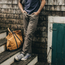 fit model leaning against the wall wearing The Slim All Day Pant in Fatigue Olive Selvage Denim