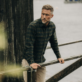 fit model leaning against a wooden railing in The Yosemite Shirt in Dark Forest Plaid