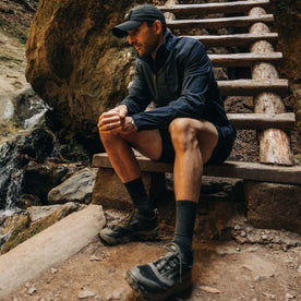 fit model sitting on stairs wearing The Deploy Packable Shell in Dark Navy