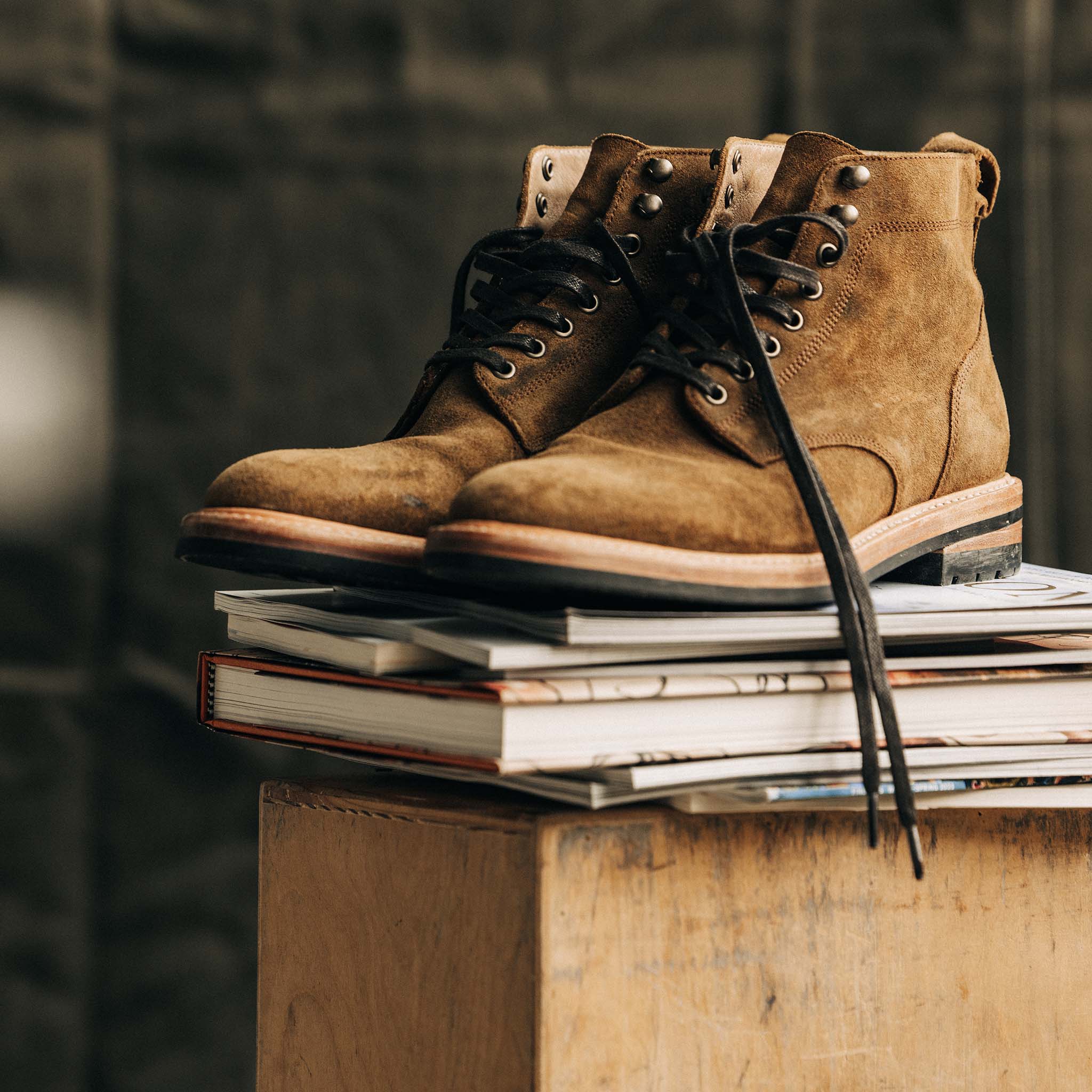 The Trench Boot in Golden Brown Waxed Suede on a stack of boots, Footwear by Taylor Stitch