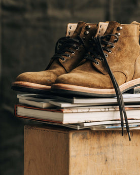 The Trench Boot in Golden Brown Waxed Suede on a stack of boots, Footwear by Taylor Stitch