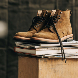 The Trench Boot in Golden Brown Waxed Suede on a stack of boots