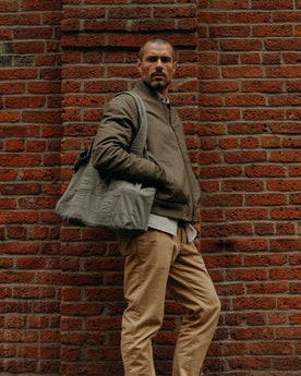 fit model leaning against the wall wearing The Foundation Tote in Organic Smoked Olive, Accessories by Taylor Stitch