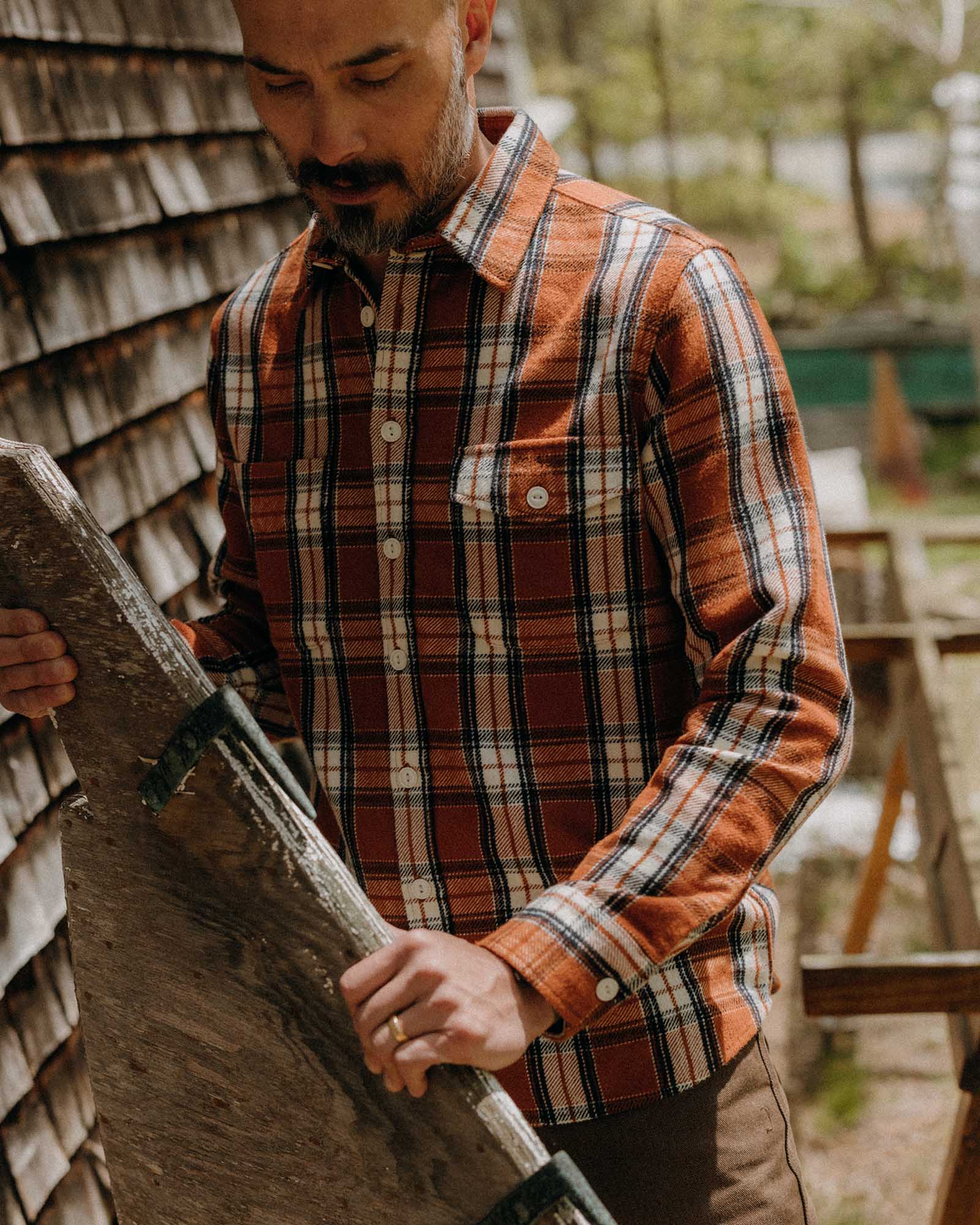 fit model holding a piece of wood wearing The Crater Shirt in Brick Plaid, Wovens by Taylor Stitch