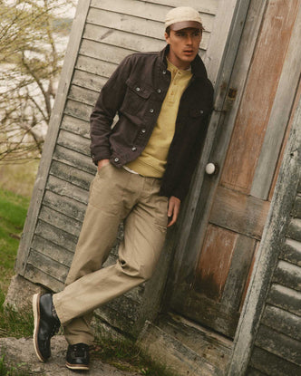 fit model leaning against the wall wearing The Breakwater Pant in Field Khaki Ripstop